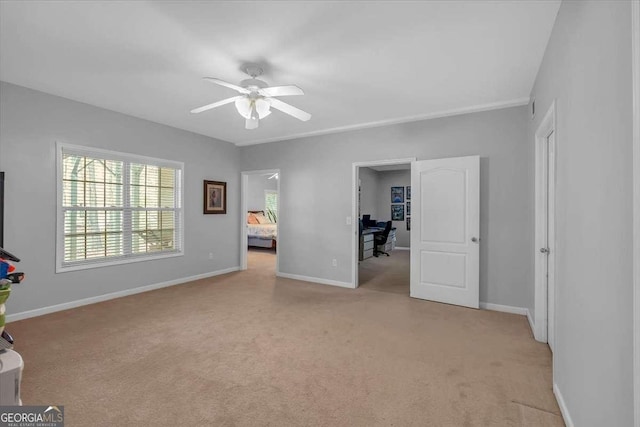 interior space with baseboards, ceiling fan, and light carpet