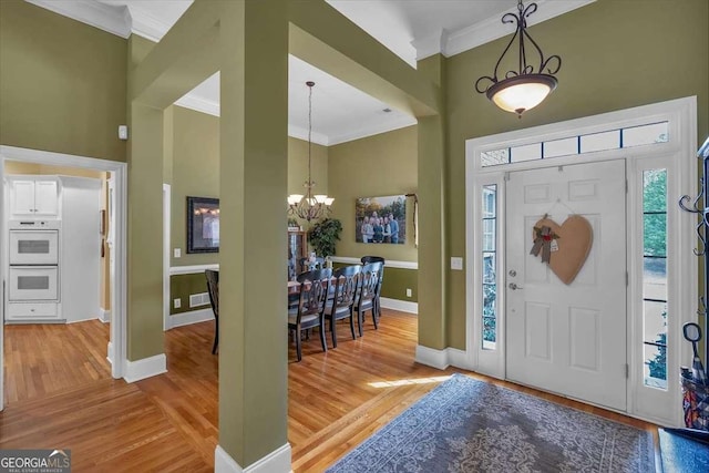 entryway with light wood finished floors, baseboards, crown molding, and an inviting chandelier