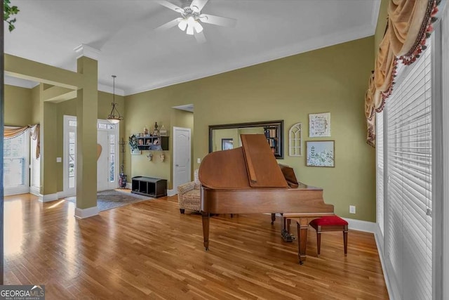 living area with baseboards, ceiling fan, wood finished floors, and crown molding