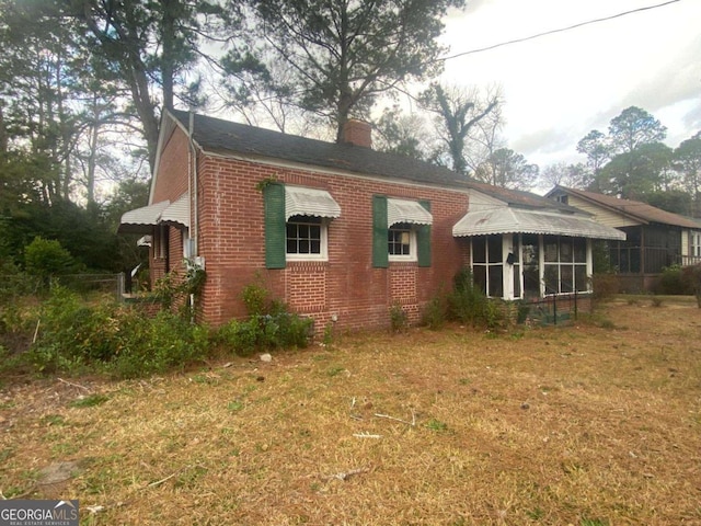 view of side of home with brick siding, a sunroom, a yard, and a chimney