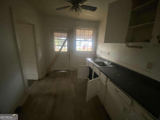 kitchen featuring a ceiling fan, a sink, dark countertops, light wood finished floors, and white cabinets