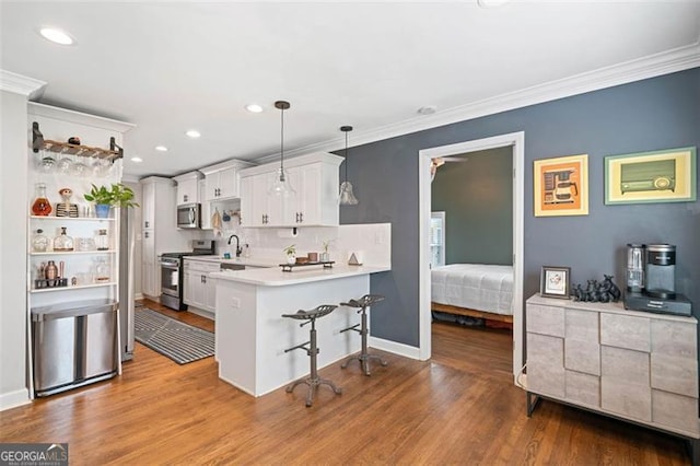kitchen featuring light countertops, a peninsula, crown molding, wood finished floors, and appliances with stainless steel finishes