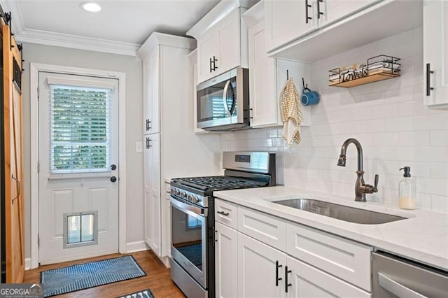 kitchen with white cabinets, light stone countertops, ornamental molding, appliances with stainless steel finishes, and a sink