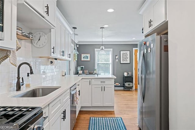 kitchen with light wood-style flooring, a peninsula, appliances with stainless steel finishes, white cabinetry, and a sink
