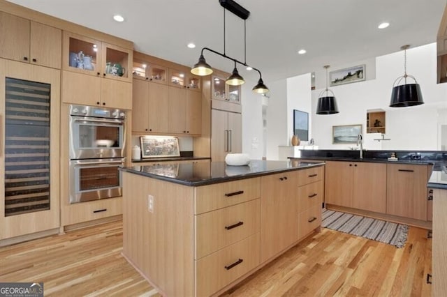 kitchen with built in refrigerator, light wood-type flooring, a kitchen island, stainless steel double oven, and light brown cabinets