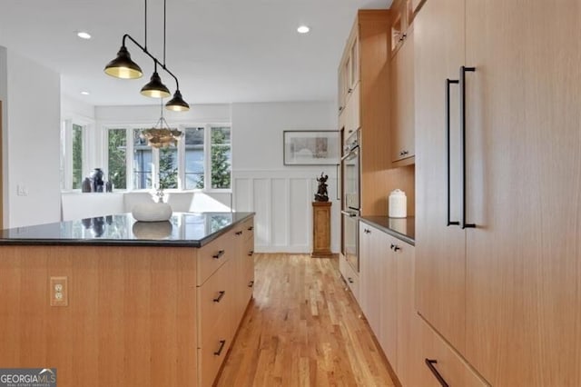 kitchen with pendant lighting, light wood-style flooring, light brown cabinetry, dark countertops, and stainless steel double oven