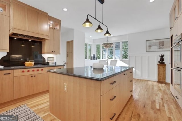kitchen featuring light wood-type flooring, glass insert cabinets, a kitchen island, decorative light fixtures, and light brown cabinetry