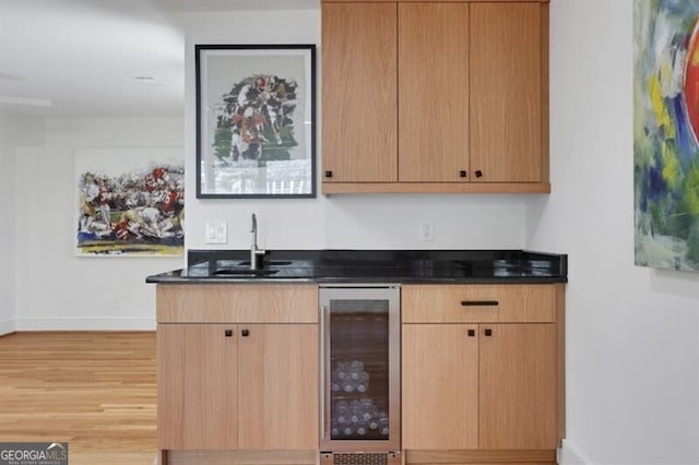 bar featuring indoor wet bar, light wood-type flooring, a sink, wine cooler, and baseboards