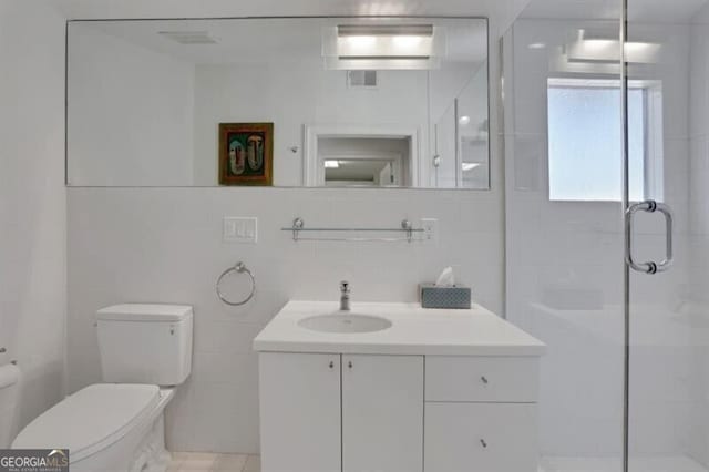 full bath featuring a shower stall, vanity, visible vents, toilet, and tile walls