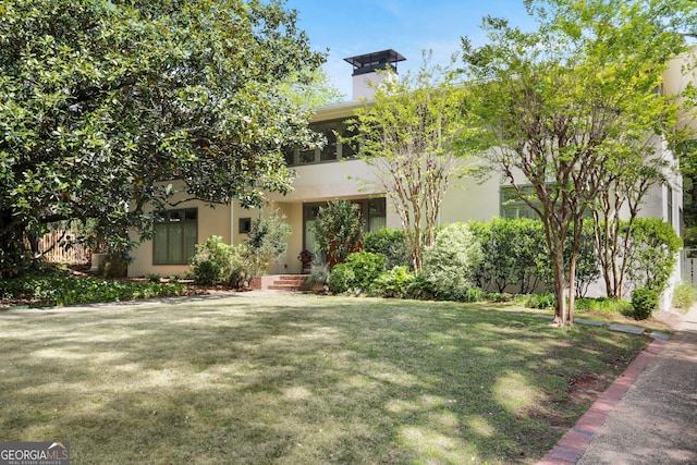 view of front of home with stucco siding, a chimney, and a front lawn