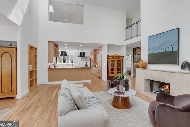 living room with light wood-type flooring, a towering ceiling, a premium fireplace, and a ceiling fan