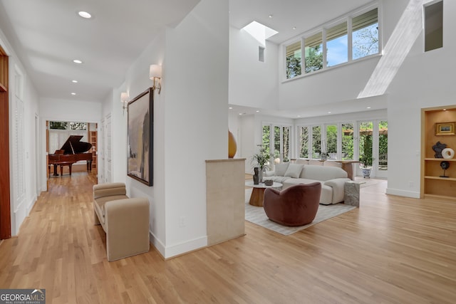 living room featuring light wood-style flooring, baseboards, a towering ceiling, and a healthy amount of sunlight