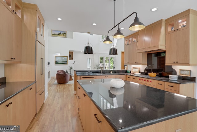 kitchen with a center island, light wood-type flooring, premium range hood, a peninsula, and dark stone counters