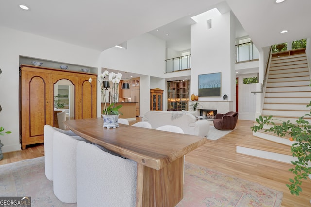 dining room with stairway, recessed lighting, light wood finished floors, a towering ceiling, and a lit fireplace