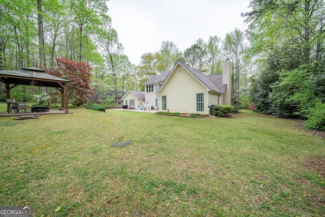 rear view of property featuring a gazebo, a chimney, a lawn, and view of scattered trees