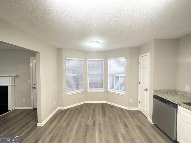 kitchen featuring wood finished floors, light stone counters, baseboards, and stainless steel dishwasher