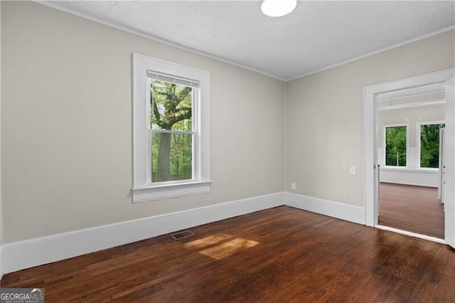 empty room with wood finished floors, ornamental molding, and a healthy amount of sunlight