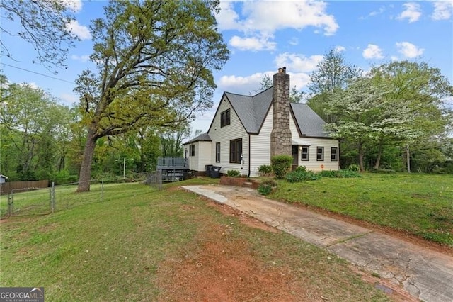 tudor-style house featuring a front yard, a chimney, fence, and concrete driveway