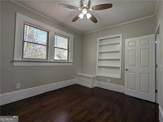 empty room with baseboards, built in features, ornamental molding, a ceiling fan, and dark wood-type flooring
