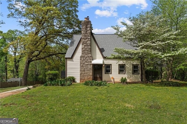 view of front facade featuring a front lawn, a shingled roof, and a chimney