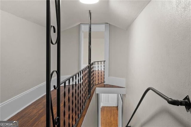 stairs with wood finished floors, a textured wall, and vaulted ceiling