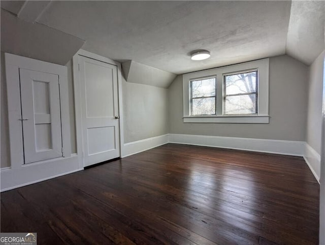 bonus room featuring baseboards, a textured ceiling, vaulted ceiling, and dark wood finished floors