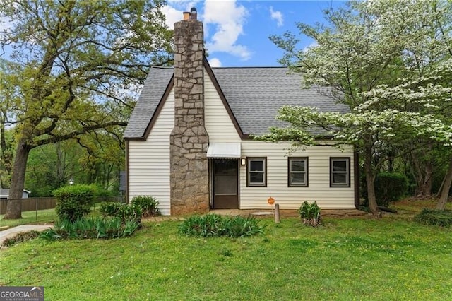 view of front of property featuring a chimney, a shingled roof, and a front lawn