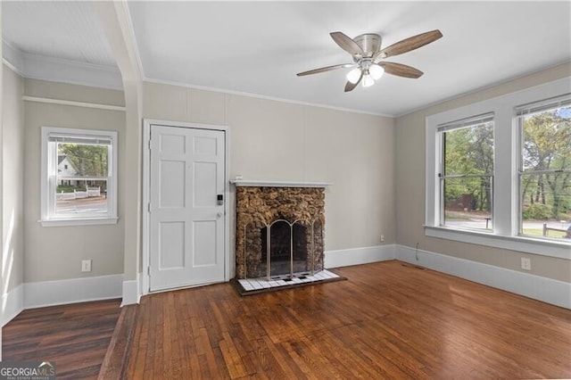 unfurnished living room featuring a stone fireplace, a wealth of natural light, ceiling fan, and wood finished floors
