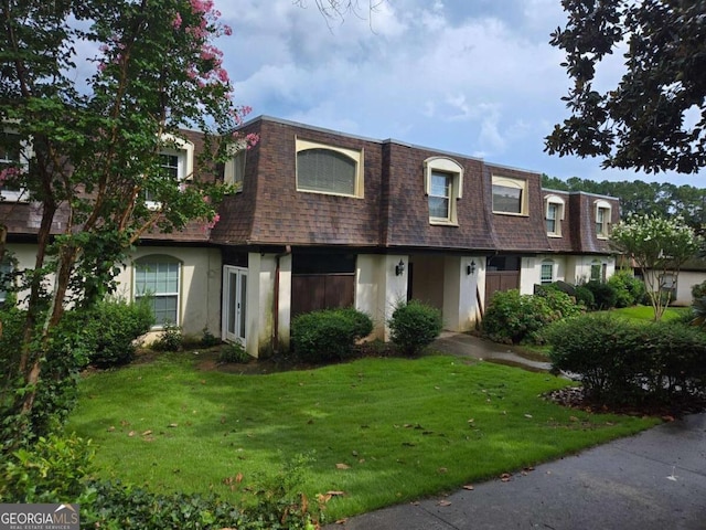 view of front of home with a front yard, stucco siding, mansard roof, and roof with shingles