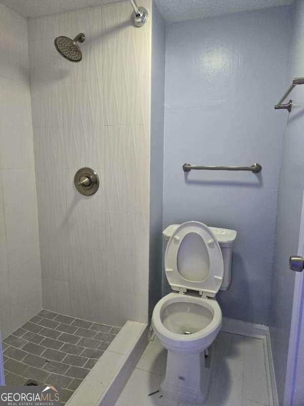 bathroom with a textured ceiling, toilet, and a shower stall