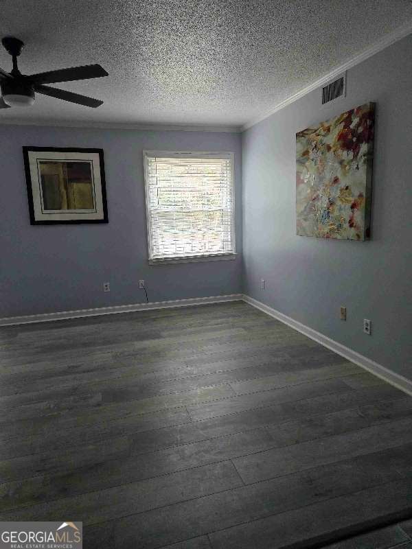 empty room featuring dark wood-type flooring, a textured ceiling, visible vents, ceiling fan, and ornamental molding