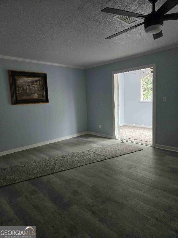 spare room with a textured ceiling, crown molding, baseboards, ceiling fan, and wood finished floors