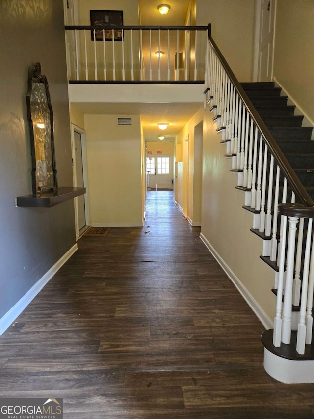 corridor with a towering ceiling, dark wood-style floors, baseboards, and stairs
