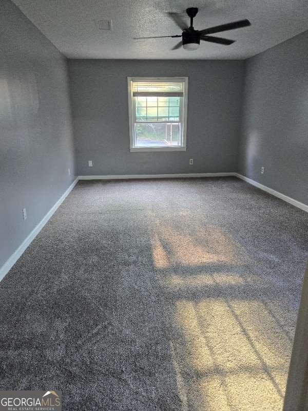 carpeted empty room with a textured ceiling, baseboards, and a ceiling fan