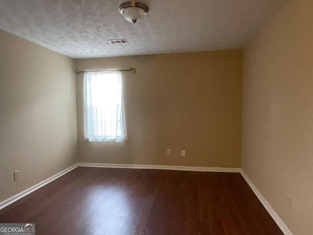 unfurnished room featuring dark wood finished floors, baseboards, and visible vents