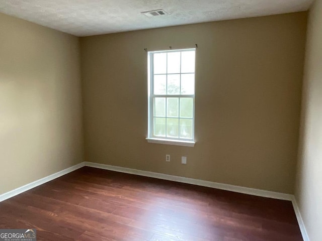 spare room featuring baseboards, visible vents, a textured ceiling, and dark wood finished floors