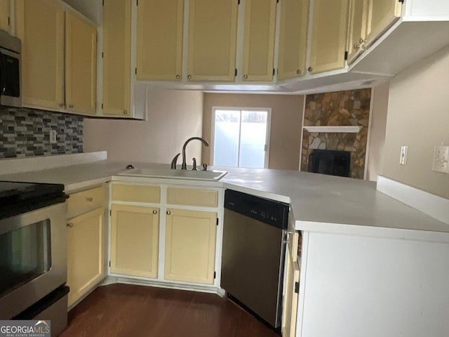kitchen featuring a sink, decorative backsplash, light countertops, a peninsula, and appliances with stainless steel finishes