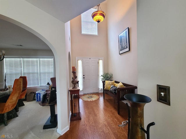 entrance foyer with arched walkways, visible vents, a towering ceiling, and wood finished floors