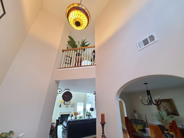 interior space featuring a fireplace, visible vents, arched walkways, a towering ceiling, and an inviting chandelier