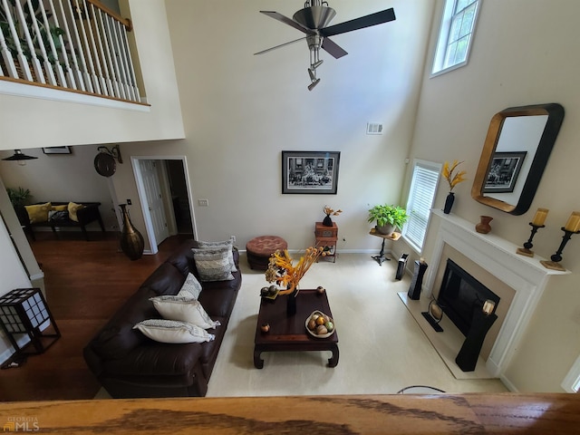 living area with a fireplace with flush hearth, ceiling fan, visible vents, and a towering ceiling