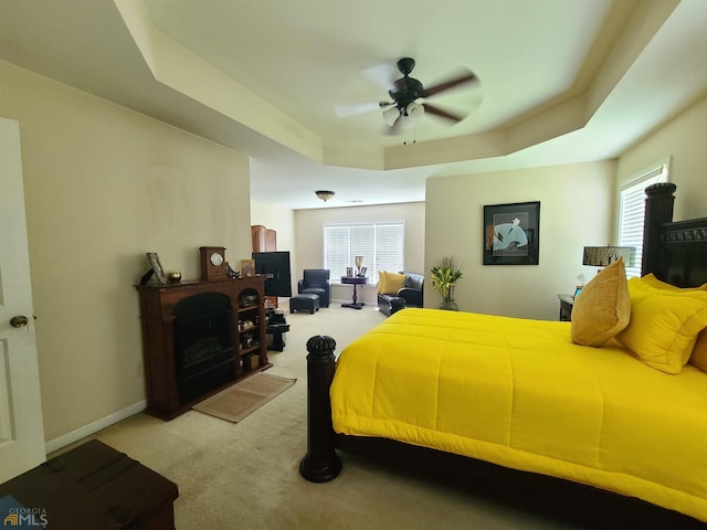 bedroom featuring light colored carpet, ceiling fan, baseboards, and a raised ceiling