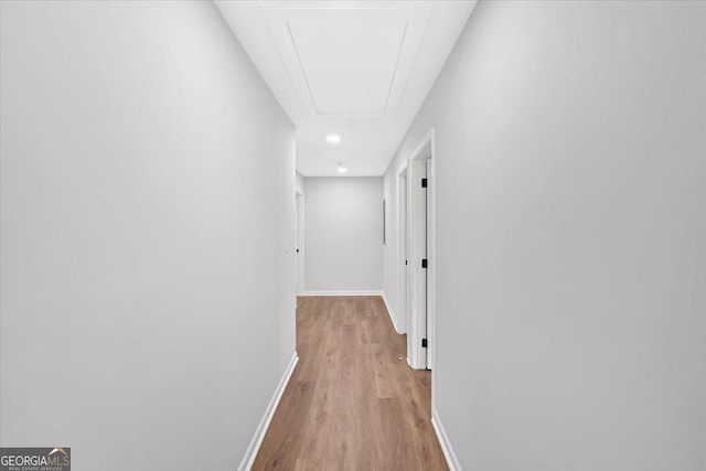corridor featuring light wood-style floors, baseboards, and attic access