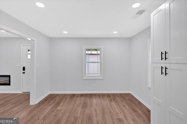 empty room featuring light wood-type flooring, baseboards, visible vents, and heating unit