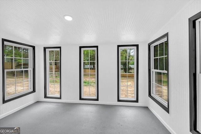unfurnished sunroom with baseboards and concrete flooring