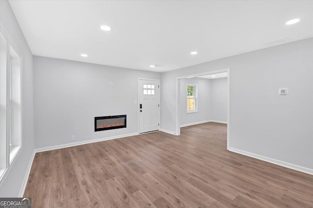 unfurnished living room with a glass covered fireplace, recessed lighting, baseboards, and wood finished floors