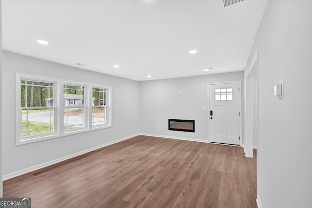 unfurnished living room featuring a glass covered fireplace, recessed lighting, baseboards, and wood finished floors