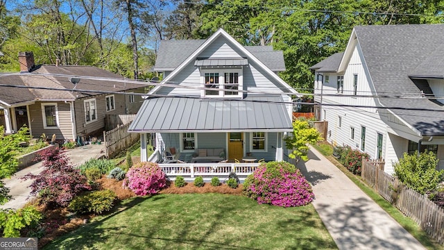 view of front of property featuring a standing seam roof, covered porch, metal roof, a front yard, and fence