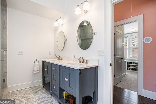 bathroom with an enclosed shower, double vanity, a sink, and baseboards