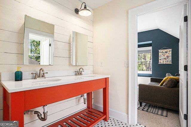 bathroom featuring a sink, double vanity, vaulted ceiling, and wooden walls
