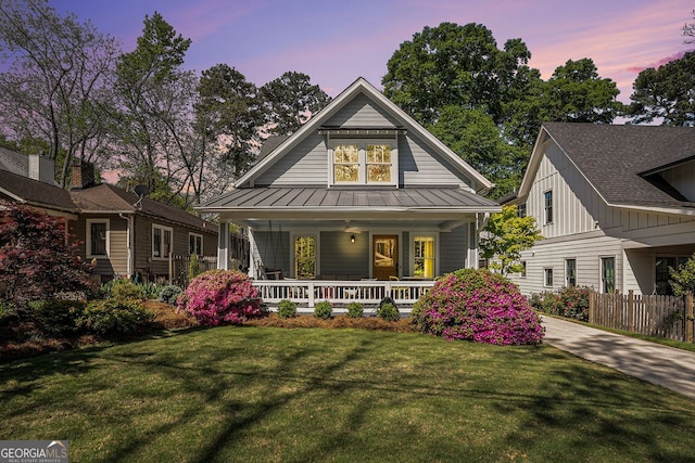 view of front of property with metal roof, a lawn, covered porch, fence, and a standing seam roof